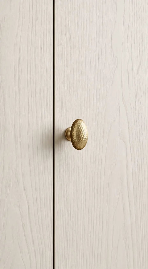 Close-up of Top Shelf Champagne Bronze Cabinet Knob with Hammered Oval Dome on light wood cabinet door surface.