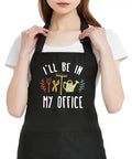 Woman wearing a Women Waterproof Adjustable Bib Apron With Two Pockets For Kitchen And Garden Durable Multi Use Apron For Cooking Gardening Barbecuing And More In Black with gardening print.