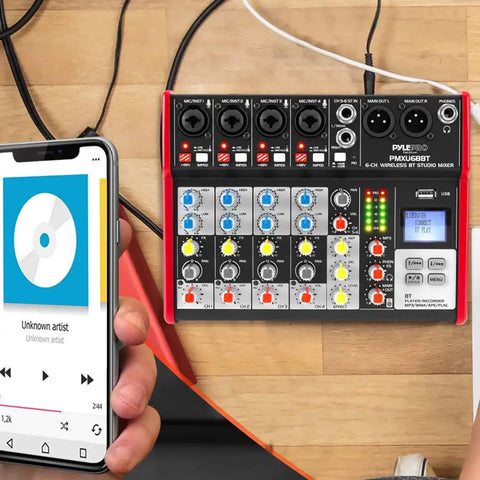 Six Channel Bluetooth DJ Mixer And USB Audio Interface For Home Studio Recording Portable Digital Mixing Console With Independent Channel Gain EQ FX Send And Master Control PMXU68BT next to a smartphone playing music.