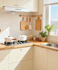 Bright kitchen setup with white pots on stove, wooden cutting boards hanging, and a plant by the window.