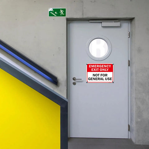2 Pack Emergency Exit Only Sign Not For General Use Clear As Day Warning Label mounted on a gray door in a commercial stairwell.