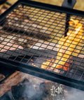 Adjustable Swivel Grill Grate for Open Fire Cooking With Spike Pole Steel Mesh Wire Grate over campfire with flames.