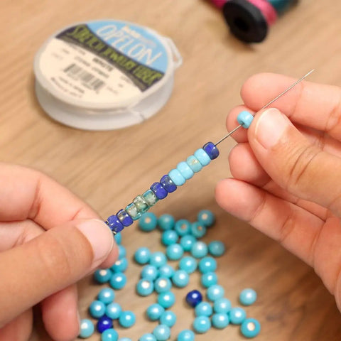 Person using Hook Eye Needle For Beading 10 Inch Long Extra Fine Bead Stringing Tool for Quick Bead Loading onto Cord.