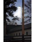 Energy Star LED Dusk To Dawn Light With 50K Hour Lifespan illuminating a barn area at night, mounted on a pole, trees in background.