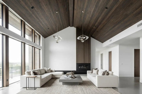 Modern living room with high ceilings, large windows, neutral sofa, and decorative ceiling fixtures.