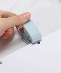 Person using a handheld hole punch on paper, creating a 6mm hole. Heavy Duty Handheld Hole Punch One Quarter Inch For Paper Craft Scrapbook Tags And Tickets.