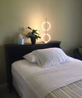 Nova Modern Arc Table Lamp with Two Circle Ring Style Pendant on nightstand beside bed in bedroom setting, brass finish.