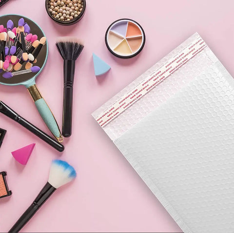 White Bubble Mailers 9.5 By 13.5 Inches Pack Of 25 Lightweight Padded Envelopes Self Seal For No Nonsense Secure Private Shipping displayed on a pink surface with makeup brushes and cosmetics.
