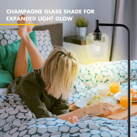 Industrial Black Floor Lamp For Living Room And Bedroom With Champagne Glass Shade illuminating a bedside scene.
