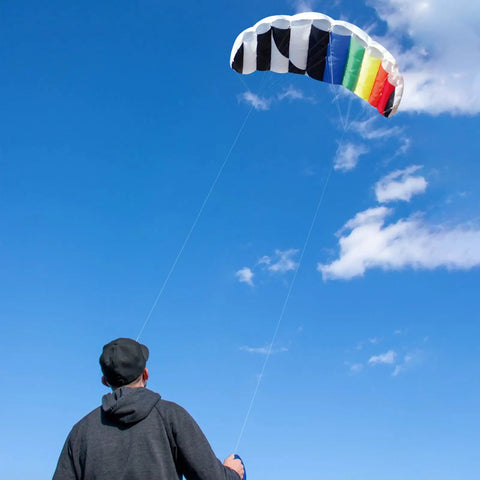 Person flying Rainbow Parafoil Kite 55 Inch Pro Stunt Soft Foil Design with 1.4 M Wing Span against a clear blue sky