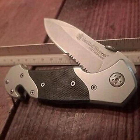 Knockout 8 Inch Folding Knife Packing A 3.3 Inch Drop Point Serrated High Carbon Stainless Blade And G10 Grip Handle on wood surface.