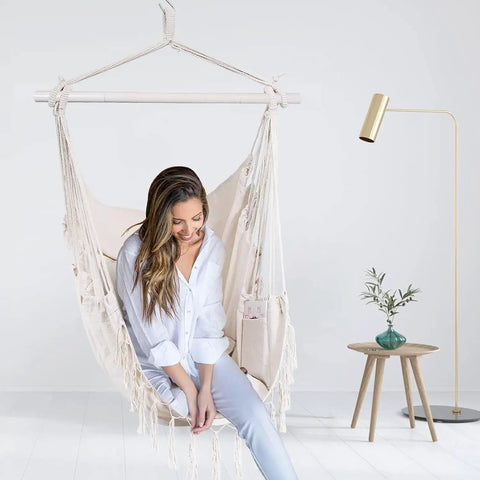 Woman sitting in a macrame boho hammock chair with rope swing, 2 cushions, for indoor and outdoor living, in a modern room.