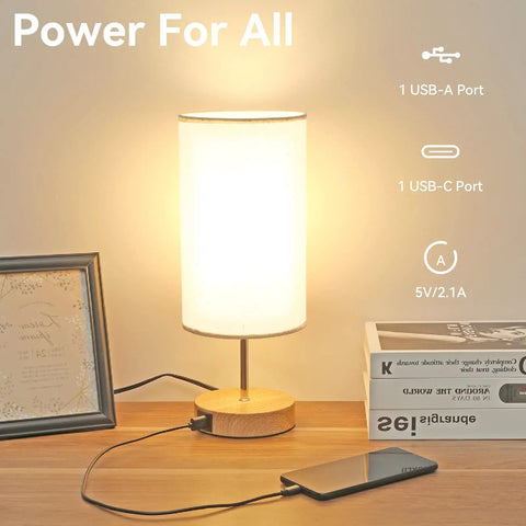 Sleek Bedside Lamp With USB C And USB A Ports, Touch Controlled Table Light next to a smartphone charging, with books and photo frame.