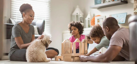 Family playing with wooden blocks on living room floor with dog, natural lighting from window in the background