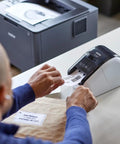 Man using Turbo Fast Label Printer For Shipping And Address Labels With Auto Cutter, Crisp 300 DPI Black And Red Output, Works With DK-2251 Label Rolls For Packages And Envelopes, Renewed to print shipping label