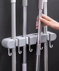 Heavy Duty Wall Mount Broom And Mop Organizer With 4 Racks And 5 Hooks in use, showing strong grips on gray wall