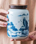 Top Shelf Airtight Ceramic Tea Canister Keeping Freshness Locked Inside Retro Blue And White Landscape Vibes held by hands.