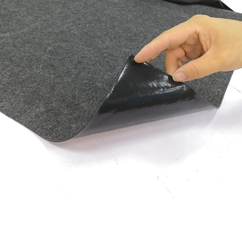 Close-up of a hand lifting the edge of the Beefy Oversized Hot Tub Mat For Spas Large 90.6 Inches By 78.7 Inches Felt Top With PVC Backing Anti Slip Waterproof Pad That Traps Mess Absorbs Oil Dirt Water And Liquid Spills Keeps Deck Dry And Clean, showing felt top and PVC backing 