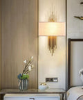 Swanky Modern Fabric Wall Sconce Featuring High Quality Shade for Soft Ambient Lighting Perfect for Bedroom Hallway and Living Room Space Super Chic Decor Piece with Eye Protection Rays and Minimalist Design That Really Slays Your Home Vibe, mounted beside nightstand with decorative plants.