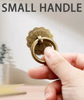 Hand holding antique brass ring pull with flower discs, small size, part of Set Of Six Antique Brass Ring Pulls For Drawers And Cabinets.