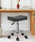 Square Rolling Stool With Footrest PU Leather 360 Degree Swivel On Wheels Height Adjustable Chair next to desk in grey.