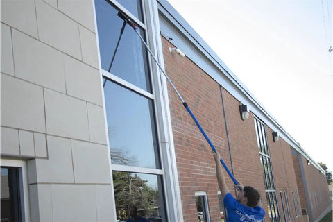 Person cleaning high windows with an extendable squeegee tool.