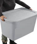 Person carrying a Six Pack Heavy Duty 30 Gallon Plastic Storage Container With Secure Lid, gray in color, ideal for home organization.