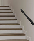 Rock Solid Four Foot Flush Handrail Wall Mount Stair Railing With Sleek Matte Black Finish and Heavy Duty Stainless Steel Design mounted on white stairs.