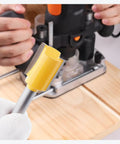 Hand holding router bit in front of a woodworking router, Pro Woodworking 100 Piece Router Bit Set With One Quarter Inch Shank Aluminum Case Tungsten Carbide Bits For Clean Cuts Durably Built Alloy Steel Ideal For Detail Edge Rabbet Grooving And Shaping Projects visible.