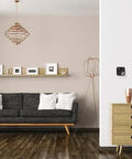 Smart Wifi Thermostat With Alexa And HomeKit Geofencing Capable on wall in modern living room with black couch and decor-snap covers.