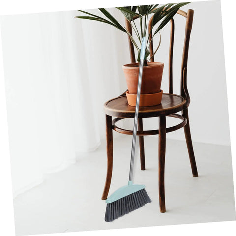 Grime Crushing Heavy Duty Broom With 34 Inch Long Handle For Sweeping Concrete Driveway Garage Patio And Indoor Floors No Sweat Household Cleaner With Convenient Storage Hook leaning against a chair with a plant.