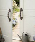 Vintage Cast Iron Door Handle Set 2 Pack Built Tough For Farmhouse Style Cabinet Pulls And Sliding Doors Fence Gates Cupboards Durable Antique Brown Finish shown on double doors in a garden setting.