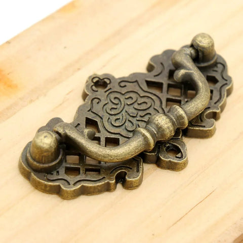 Image of a vintage antique brass bail pull handle mounted on wood, features a decorative hollowed pattern, part of 4 pack, 2.6x1.5 inches, zinc alloy.