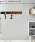 Magnetic glasses holder with three clips attached to a wooden strip on a wall in a modern room setting.