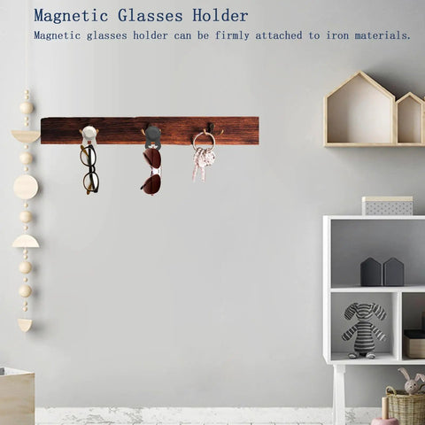 Magnetic glasses holder with three clips attached to a wooden strip on a wall in a modern room setting.