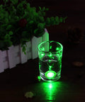 Glass with green LED light nearby a plant on a dark surface