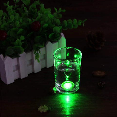 Glass with green LED light nearby a plant on a dark surface