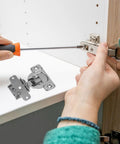 Person installing concealed cabinet hinges with soft close inset folding box hinges, using screwdriver for cabinet repair.