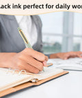 Person using 5 Pack Gel Pens 0.5mm Retractable Quick Dry Black Ink Fine Point Rolling Ball Gel Pens For Smooth Writing No Bleed Go To Journaling Note Taking Home School Office on notebook next to computer in an office setting.