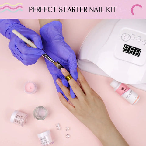Beginner Friendly Acrylic Nail Starter Kit in use, with brush, clear pink powder, monomer liquid, dappen dish, and lamp on table.