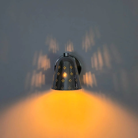 Silver Brass Wall Sconce, Mid Century Cone Lamp, Perforated Spotlight casting warm light and intricate shadows on a wall.