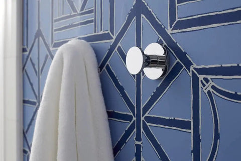 Modern chrome wall hook holding a white towel against a patterned blue wall in a sleek bathroom setting.