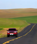 Red truck labeled 'FARM USE' driving on a winding road through lush green fields and hills.