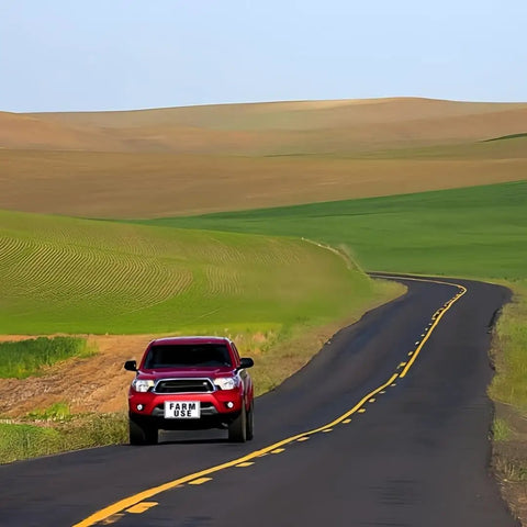 Red truck labeled 'FARM USE' driving on a winding road through lush green fields and hills.
