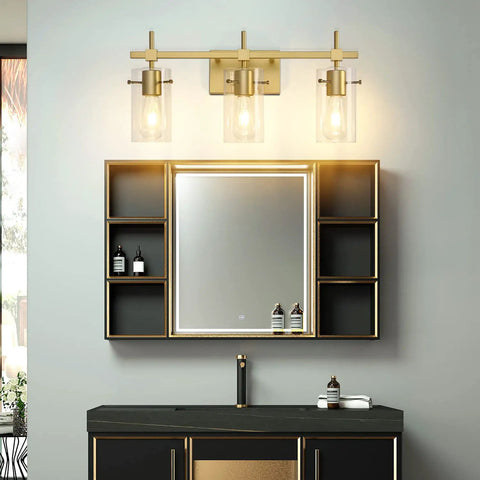 Gold Three Light Bathroom Vanity Fixture Set above mirror on dark wall, showcasing LED bulbs in clear globes, modern style setup.