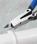 Precision flush cutters cutting white plastic, featuring blue handles, ideal for electronics and DIY projects up to 14 gauge copper.