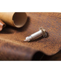 Cricut knife blade and drive housing, silver metal, side view resting on brown leather surface