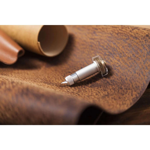 Cricut knife blade and drive housing, silver metal, side view resting on brown leather surface