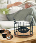 Coffee Pods Holder For Countertop With Wood Base, sturdy pod storage basket on table with K-Cups nearby, black frame, frost texture.