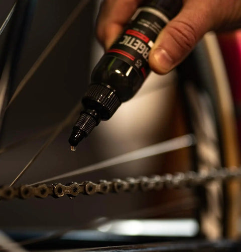 Hand applying Synergetic Bike Chain Lube Wet Lube 2oz Bottle With Premium Synthetic Oil And ZDDP WS2 Blend to bicycle chain